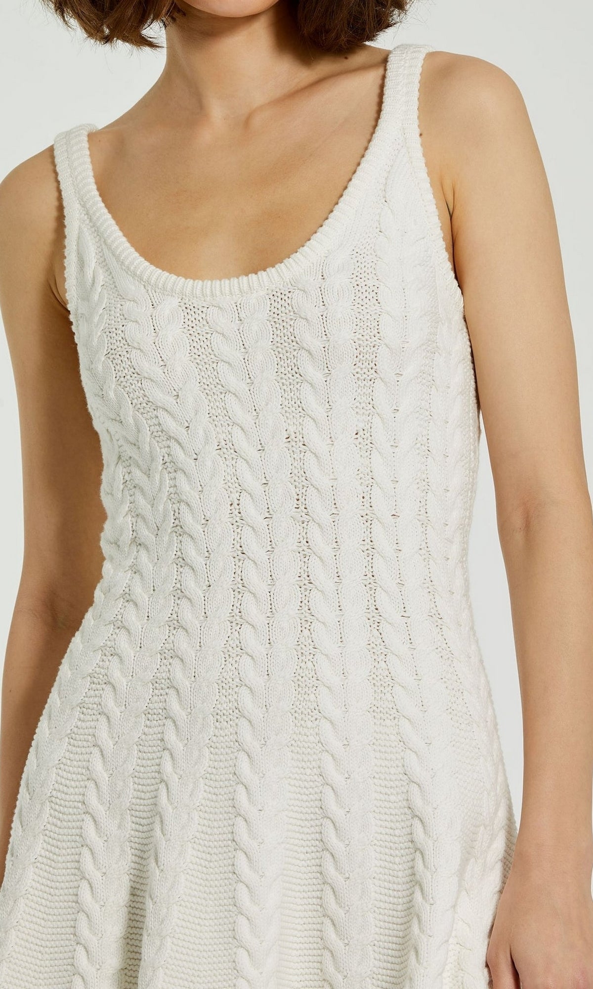A woman wears the Designer Short Knit Dress K12004 by Mac Duggal, featuring a sleeveless, white chunky knit design, shown from shoulders to waist.
